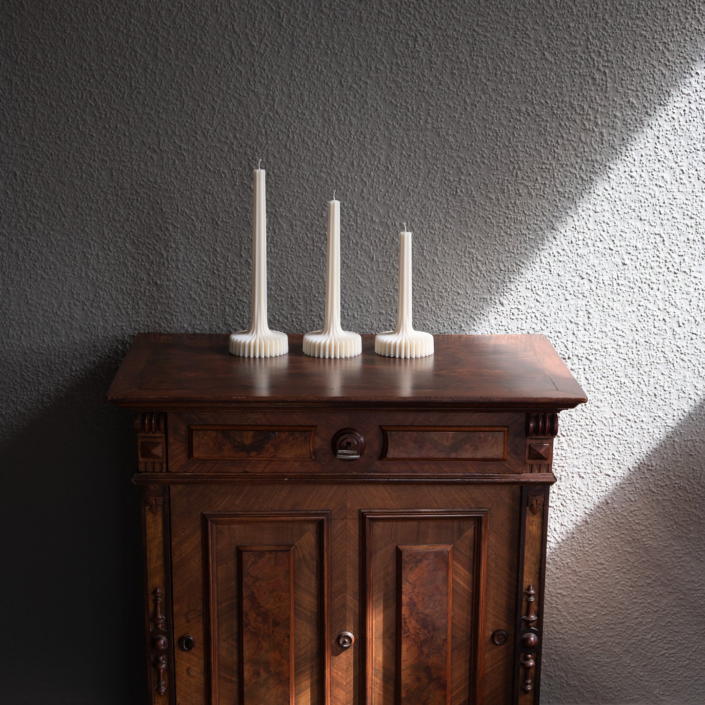 Kerzen Set Fylda in natürlichem Cremeton – skulpturale Designkerzen, Rapswachs, handgefertigt in Hamburg, 100 % pflanzlich & nachhaltig. Studio Z. Dreier Set mit aufstrebendem Stiel und skulpturalem Plateau. Dekoriert auf barocker Kommode nebeneinander im Schatten-Lichtspiel der Sonne vor grauer Wand.