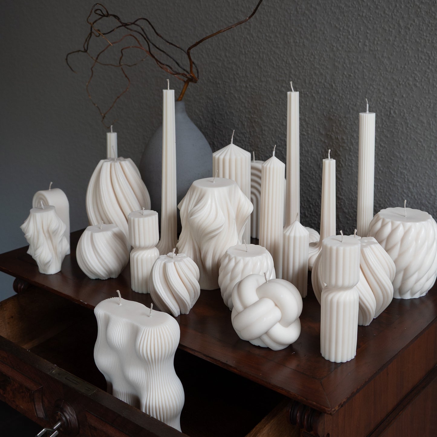 Verschiedene Kerzen Studio Z in natürlichem Cremeton – skulpturale Designkerzen und Stumpenkerzen, Rapswachs, handgefertigt in Hamburg, 100 % pflanzlich & nachhaltig. Dekoriert auf barocker Kommode mit Vase. Væg Bøluna Slør farverig knøt knøv blocka bølge lys