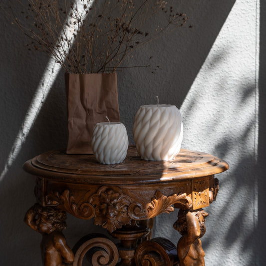 Zweier Kerzen-Set Knøv in natürlichem Cremeton – skulpturale Designkerzen, Rapswachs, handgefertigt in Hamburg, 100 % pflanzlich & nachhaltig. Studio Z. Wellenstruktur, bauchig, gewebt. Dekoriert auf barockem Tisch im Schatten-Lichtspiel der Sonne mit Vase.
