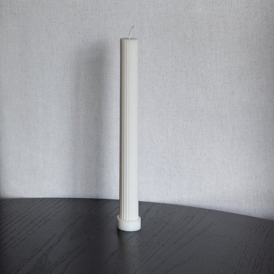 Kerze Lys, geradlininge Stumpenkerze in natürlichem Cremeton – geriffelte längliche Designkerzen, Rapswachs, handgefertigt in Hamburg, 100 % pflanzlich & nachhaltig. Studio Z. Dekoriert auf schwarzem Tisch vor hellem  Hintergrund.