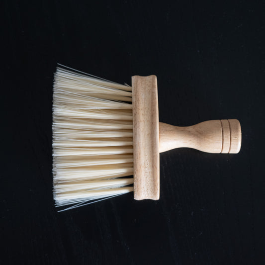 Pflegebürste mit Holzgriff zum Entfernen von Ruß und Staub liegend auf schwarzem Tisch.