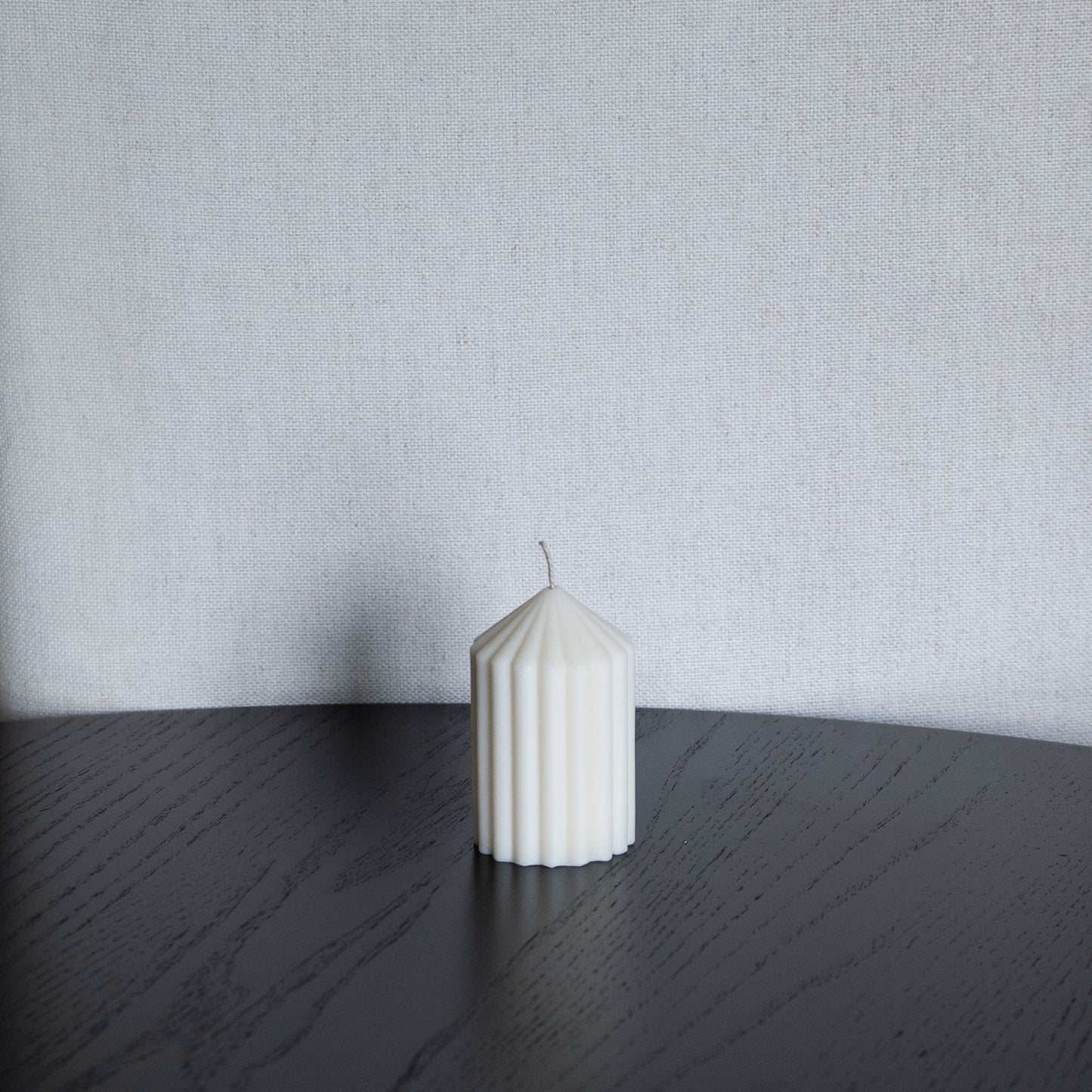 Blocka Kerze in natürlichem Cremeton – skulpturale Designkerzen, Rapswachs, handgefertigt in Hamburg, 100 % pflanzlich & nachhaltig. Studio Z. kleine Stumpenkerzen in Riffelstruktur. Dekoriert auf schwarzer Fläche vor Leinenstuhl.