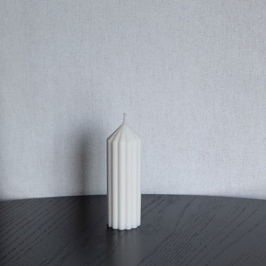 Blocka Kerze Größe S in natürlichem Cremeton – skulpturale Designkerzen, Rapswachs, handgefertigt in Hamburg, 100 % pflanzlich & nachhaltig. Studio Z. Geriffelte Stumpenkerze. Dekoriert auf schwarzem Tisch vor Leinenstuhl.