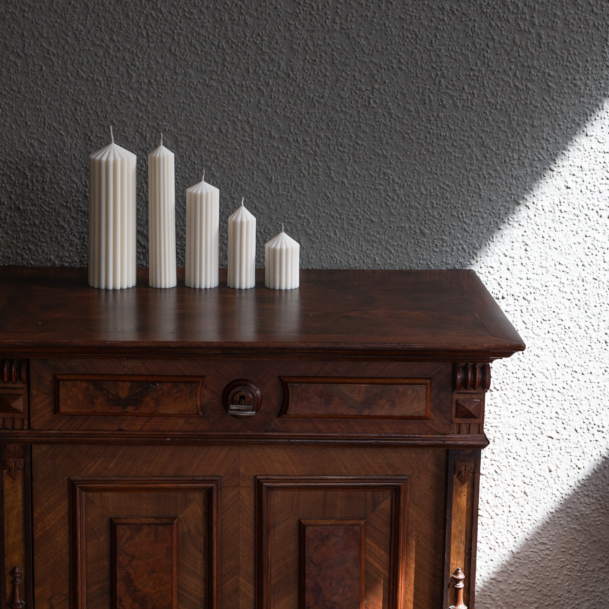 Kerzen Set Blocka in natürlichem Cremeton – skulpturale Designkerzen, Rapswachs, handgegossen in Hamburg, 100 % pflanzlich & nachhaltig. Studio Z. Riffelstruktur. Stumpenkerze. Dekoriert auf barocker Kommode im Schatten-Lichtspiel der Sonne.
