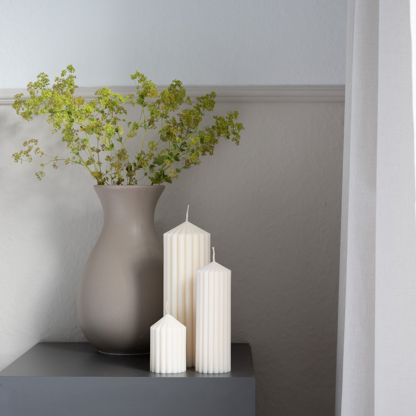 Kerzen Set Blocka in natürlichem Cremeton – skulpturale Designkerzen, Rapswachs, handgegossen in Hamburg, 100 % pflanzlich & nachhaltig. Studio Z. Riffelstruktur. Stumpenkerze. Dekoriert auf grauem Tisch vor taupefarbener Vase neben Leinenvorhang.