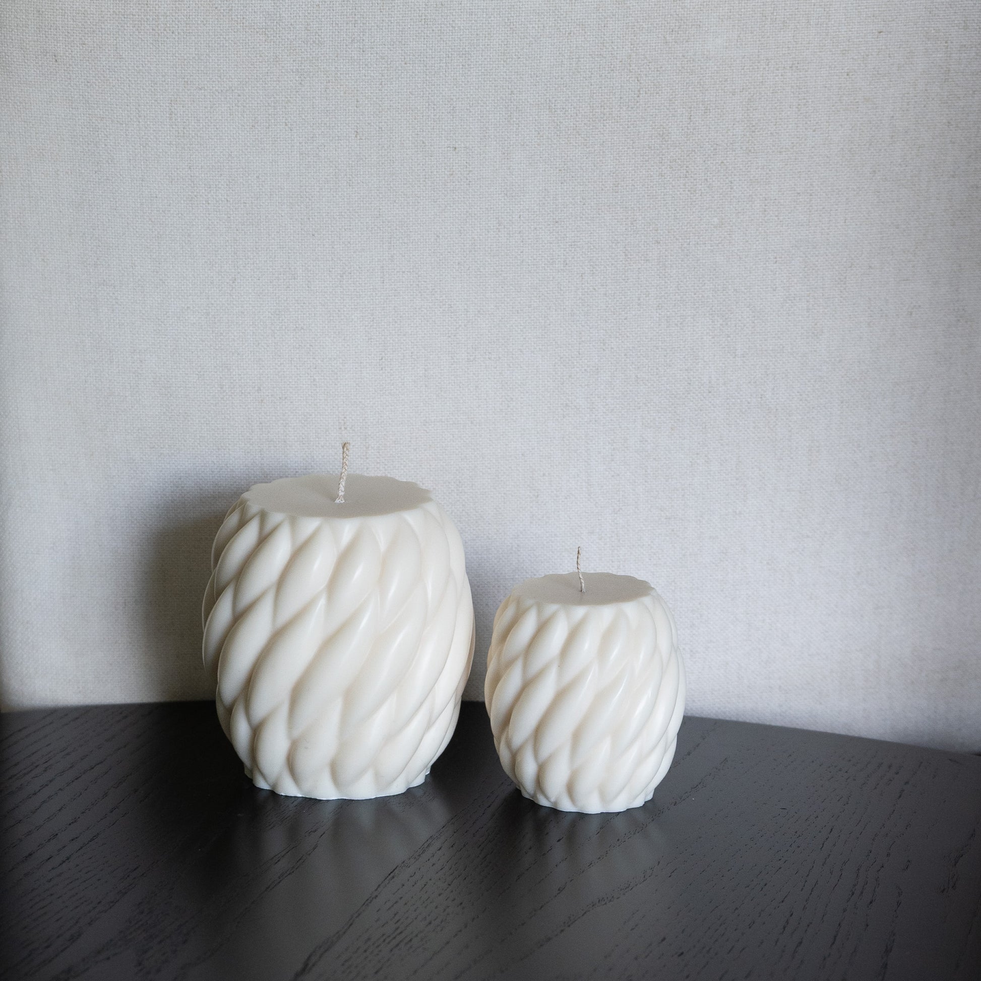 Zweier Kerzen-Set Knøv in natürlichem Cremeton – skulpturale Designkerzen, Rapswachs, handgefertigt in Hamburg, 100 % pflanzlich & nachhaltig. Studio Z. Wellenstruktur, bauchig, gewebt. Dekoriert auf schwarzem Tisch vor hellem Hintergrund.