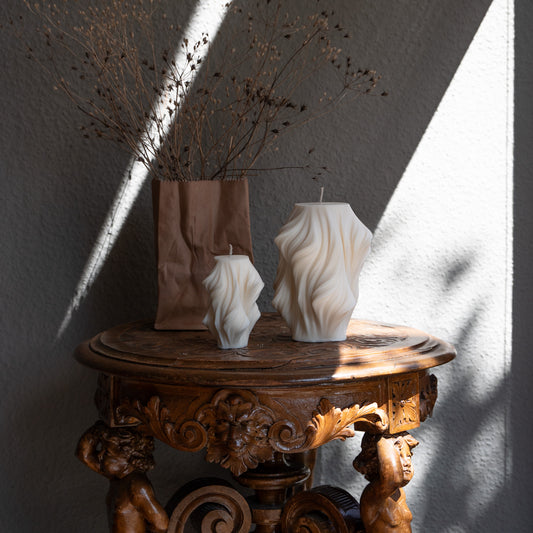 Skulpturale Kerze in Naturfarbe. Handgefertigt in Hamburg – Statement-Dekor im dänischen Design. 100 % natürliche, nachhaltige Materialien. Jedes Stück ein Unikat. Schleier Optik. Dekoriert auf barockem Tisch im Schattenspiel der Sonne neben dekorativer Vase.