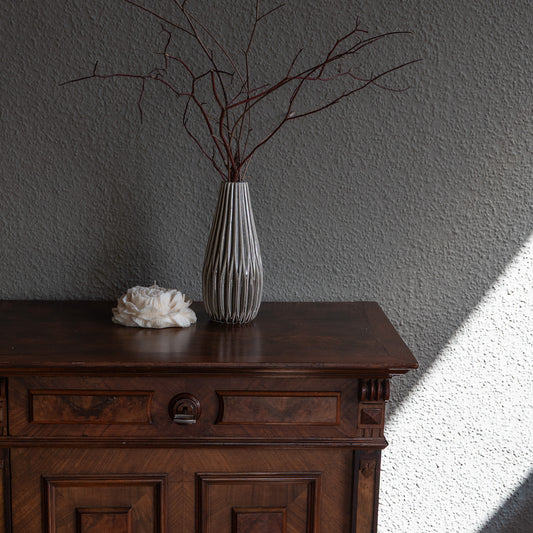 Kerze Bløma in großer Pfingstrosenform, große Blüte in natürlichem Cremeton, Designkerzen, Rapswachs, handgefertigt in Hamburg, 100 % pflanzlich & nachhaltig. Studio Z. Dekoriert auf barockem Tisch vor grauer Wand neben geriffelter hoher Vase in grau mit Ästen.