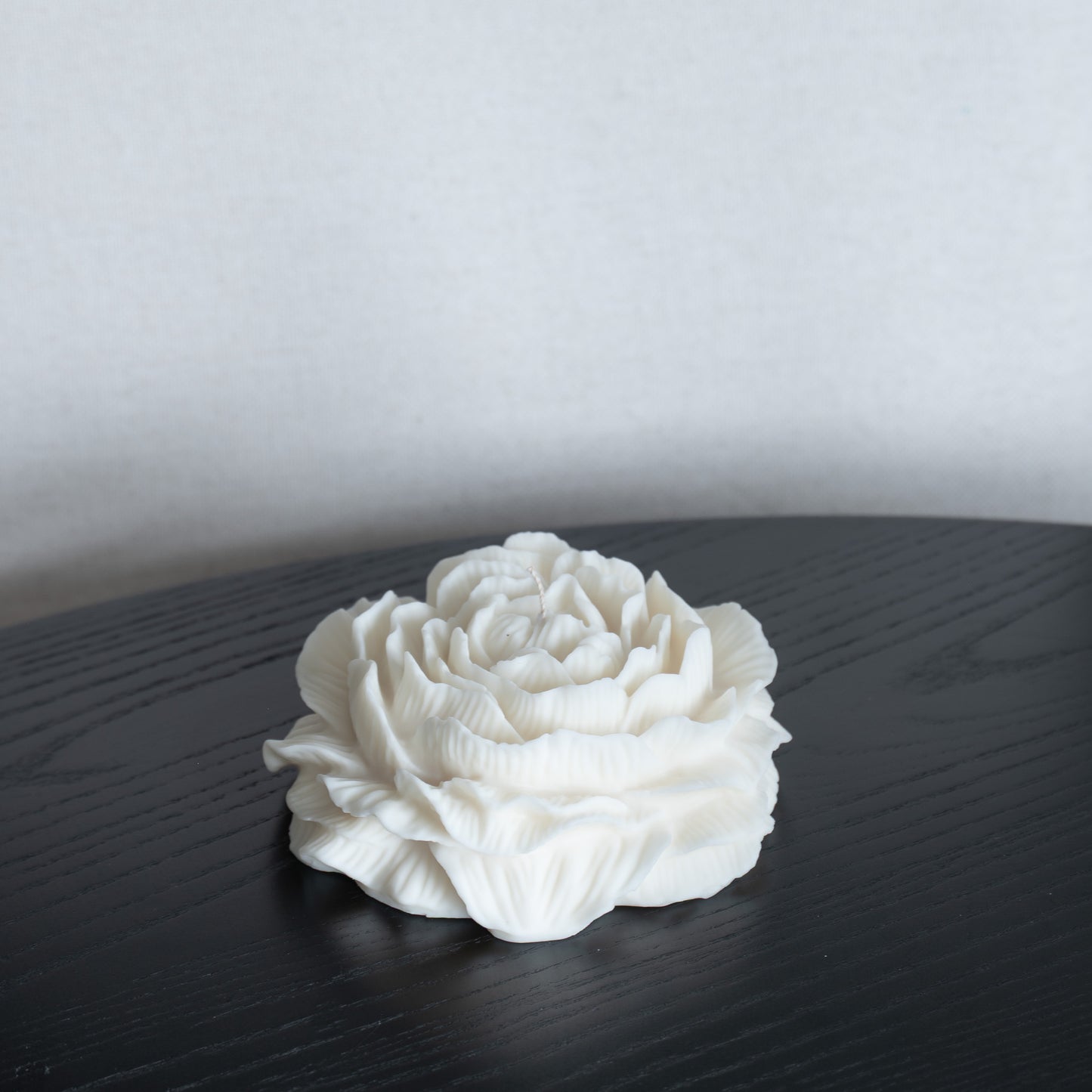 Kerze Bløma in großer Pfingstrosenform, große Blüte in natürlichem Cremeton, Designkerzen, Rapswachs, handgefertigt in Hamburg, 100 % pflanzlich & nachhaltig. Studio Z. Dekoriert auf schwarzem Tisch vor hellem Hintergrund.