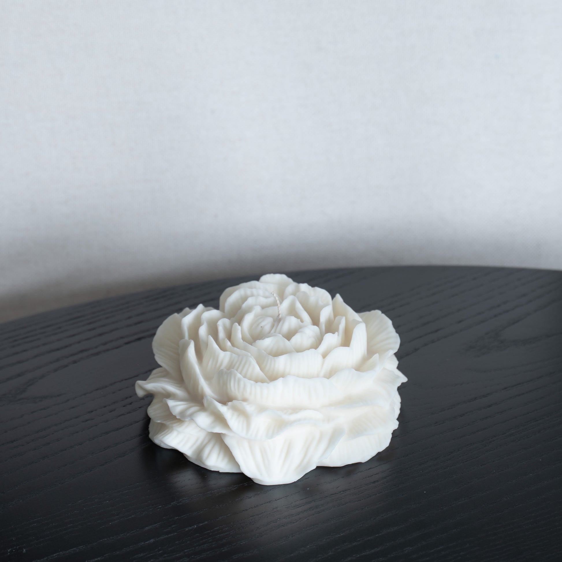 Kerze Bløma in großer Pfingstrosenform, große Blüte in natürlichem Cremeton, Designkerzen, Rapswachs, handgefertigt in Hamburg, 100 % pflanzlich & nachhaltig. Studio Z. Dekoriert auf schwarzem Tisch vor hellem Hintergrund.