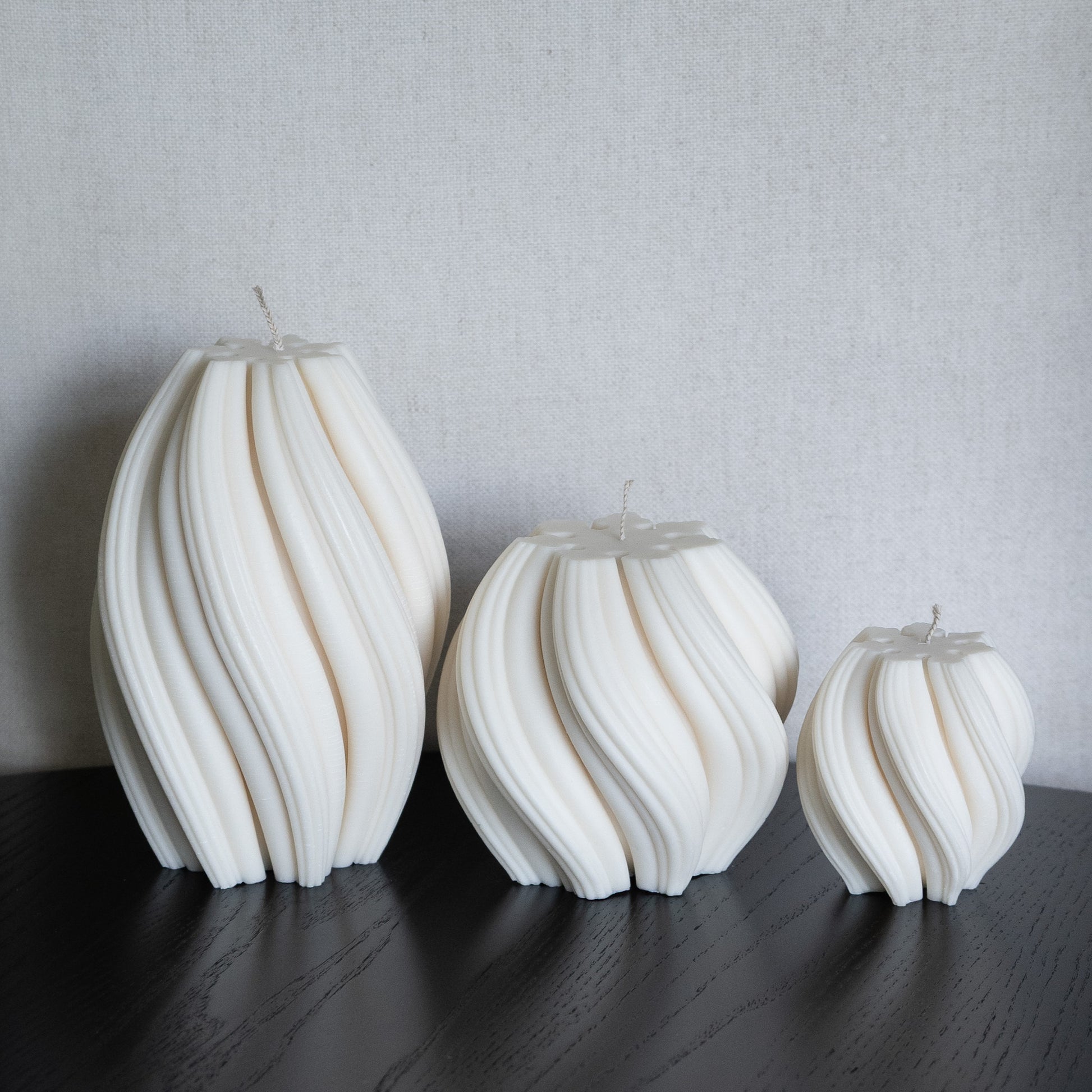 3er Kerzen Set Bøluna in natürlichem Cremeton – skulpturale Designkerzen, Rapswachs, handgefertigt in Hamburg, 100 % pflanzlich & nachhaltig. Studio Z. Stumpenkerzen in Wellenform, geschwungen und bauchig. Dekoriert auf schwarzem Tisch.