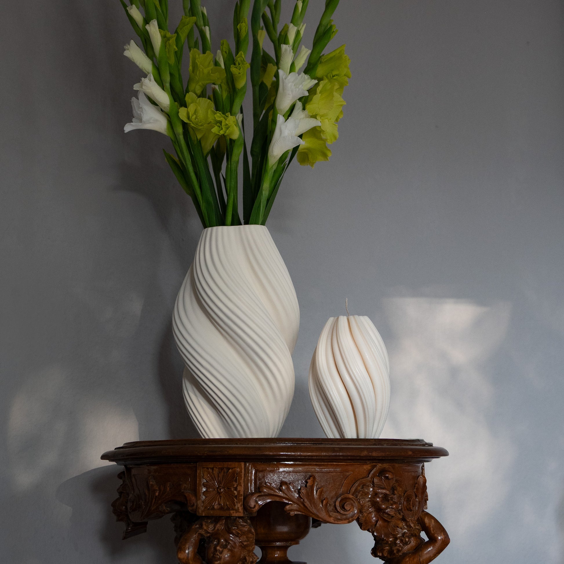 Kerze Boluna in natürlichem Cremeton – skulpturale Designkerzen, Rapswachs, handgefertigt in Hamburg, 100 % pflanzlich & nachhaltig. Studio Z. Wellenstruktur. Dekoriert auf barockem Tisch im Schatten-Lichtspiel der Sonne mit Vase.