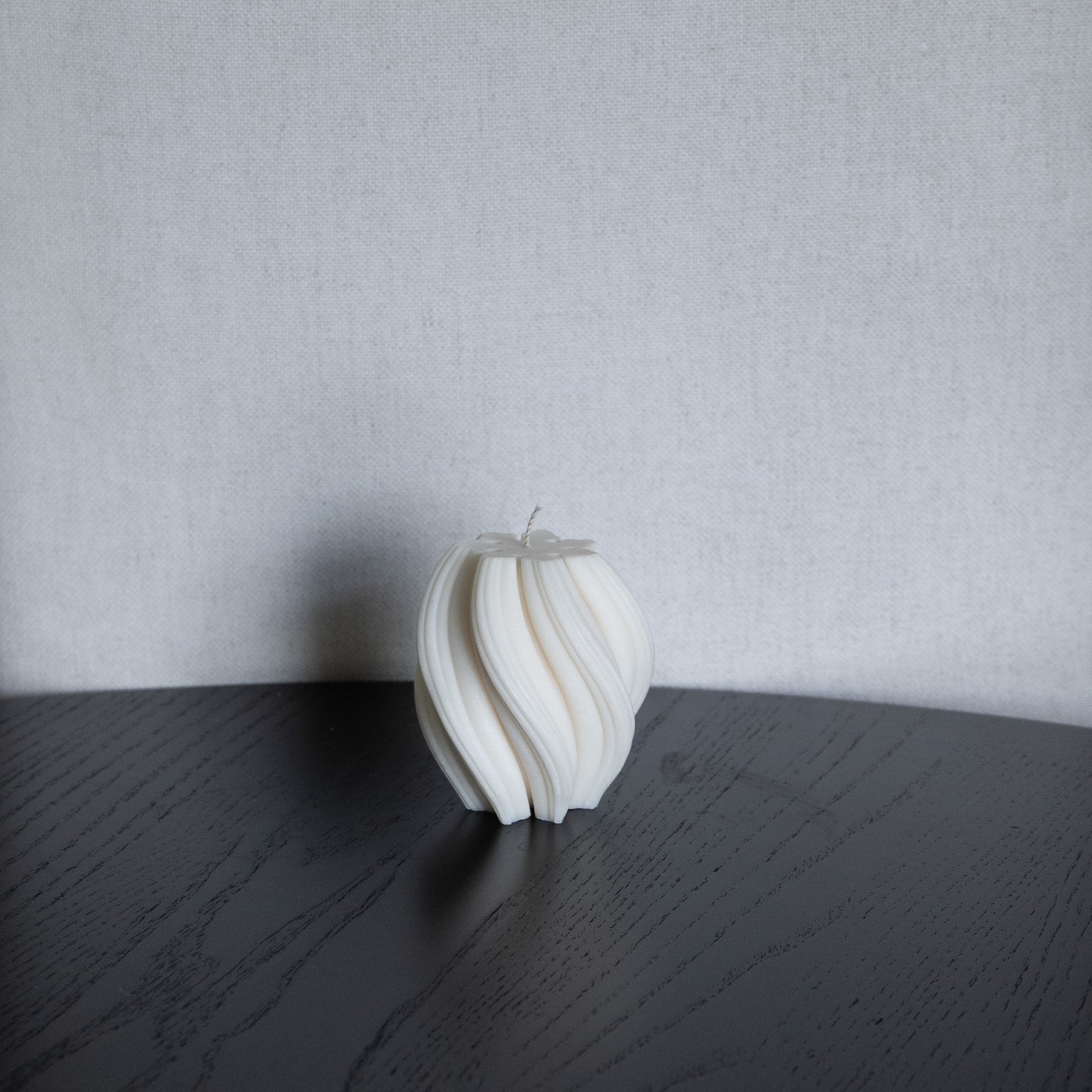Kerze Boluna in natürlichem Cremeton – skulpturale, bauchige Designkerzen, Rapswachs, handgefertigt in Hamburg, 100 % pflanzlich & nachhaltig. Studio Z. Wellenstruktur. Dekoriert auf schwarzem Tisch vor Leinenstruktur.