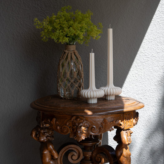 Skæva Kerze in natürlichem Cremeton – skulpturale Designkerzen aus Rapswachs, handgefertigt in Hamburg, 100 % pflanzlich & nachhaltig. Studio Z. Mit plissierter Struktur, markantem Fuß und skulpturaler Form. Dekoriert auf barockem Tisch im Schattenspiel der Sonne neben Vase mit Fraenmantelkraut.