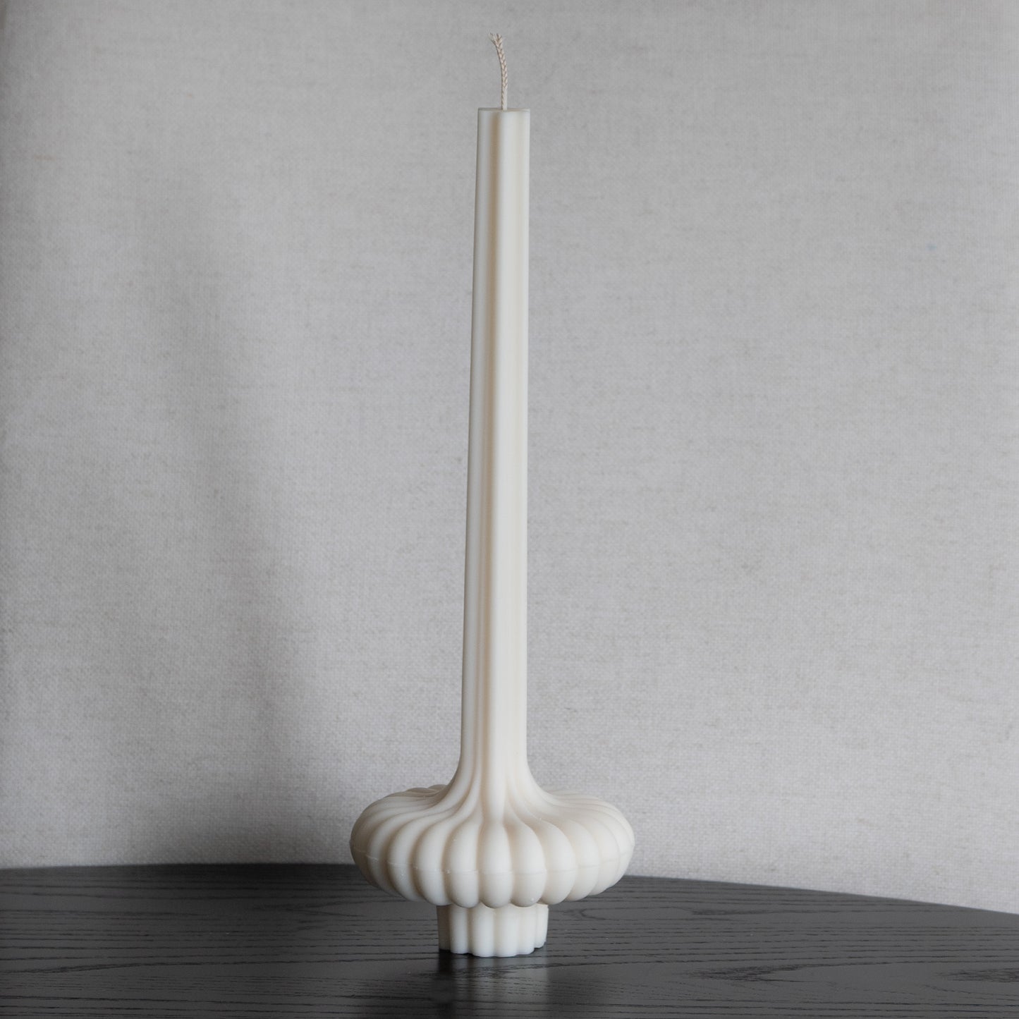 Skæva Kerze in natürlichem Cremeton – skulpturale Designkerzen aus Rapswachs, handgefertigt in Hamburg, 100 % pflanzlich & nachhaltig. Studio Z. Mit plissierter Struktur, markantem Fuß und skulpturaler Form. Dekoriert auf schwarzem Tisch im vor Leinenstruktur.