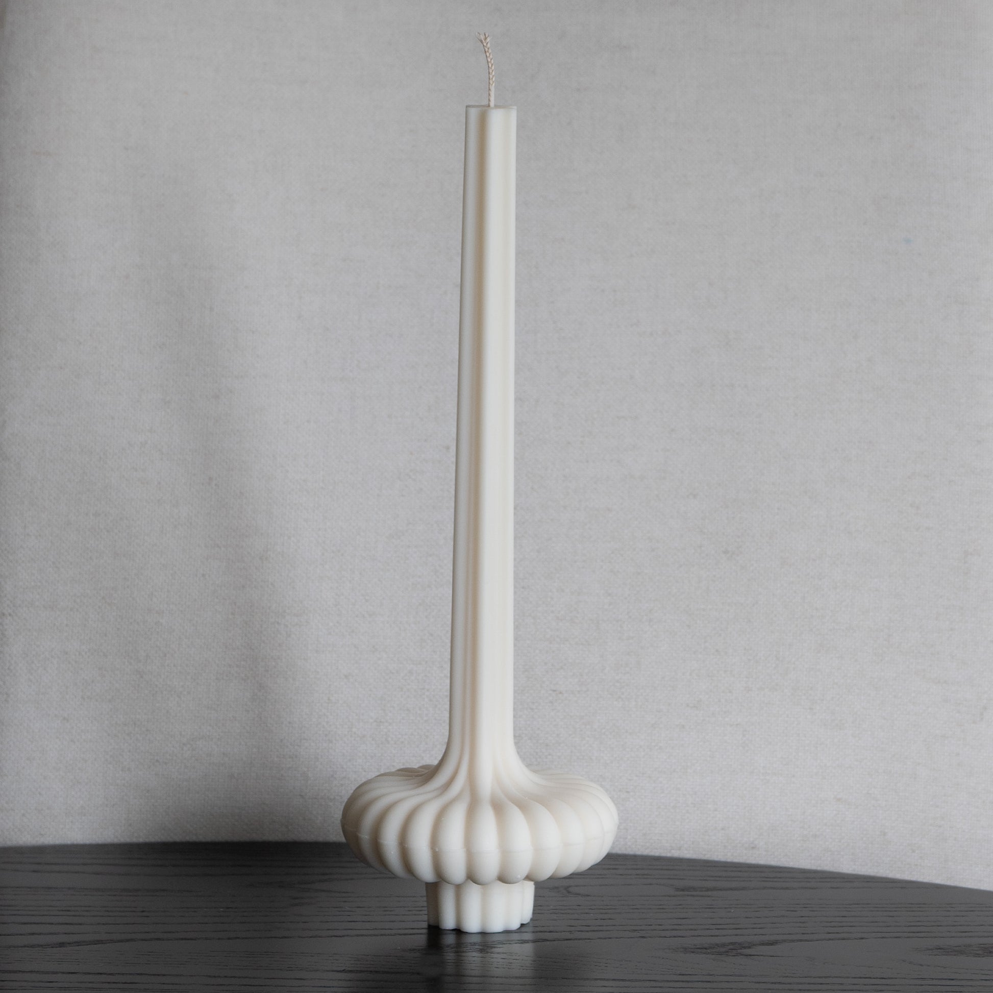 Skæva Kerze in natürlichem Cremeton – skulpturale Designkerzen aus Rapswachs, handgefertigt in Hamburg, 100 % pflanzlich & nachhaltig. Studio Z. Mit plissierter Struktur, markantem Fuß und skulpturaler Form. Dekoriert auf schwarzem Tisch im vor Leinenstruktur.