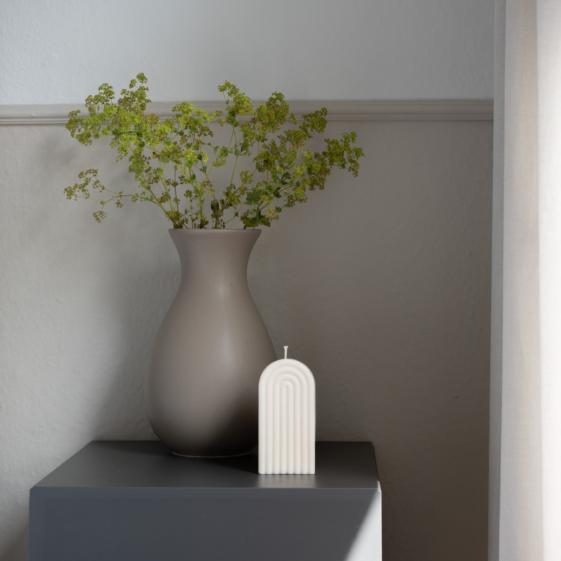 Kerze Farverig in natürlichem Cremeton – skulpturale Regenbogen Designkerzen, Rapswachs, handgefertigt in Hamburg, 100 % pflanzlich & nachhaltig. Studio Z. Dekoriert auf grauem Tisch im Schatten-Lichtspiel der Sonne mit Vase.