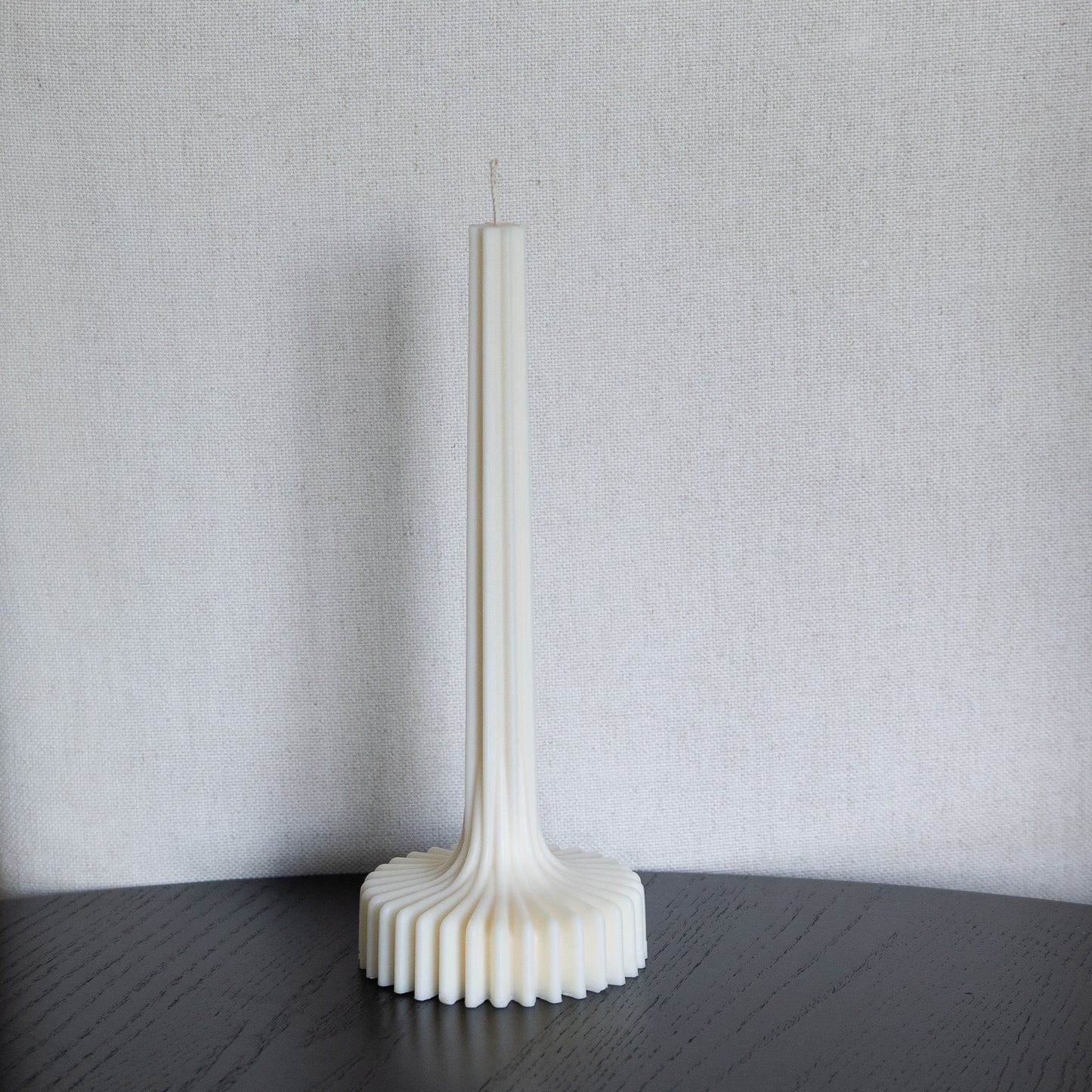 Kerze Fylda, plissierte Stabkerze in natürlichem Cremeton – skulpturale längliche Designkerzen, Rapswachs, handgefertigt in Hamburg, 100 % pflanzlich & nachhaltig. Studio Z. Geriffelte Struktur mit Plateaufuß, dekoriert auf schwarzem Tisch vor hellem Hintergrund.