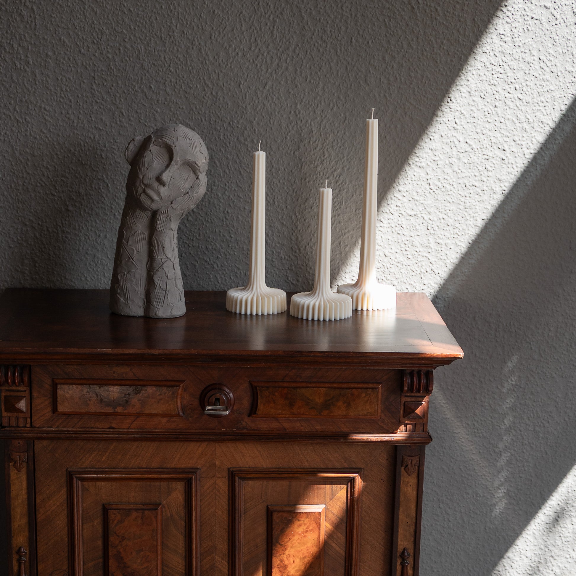 Dreier Kerzen Set Fylda in natürlichem Cremeton – skulpturale Designkerzen, Rapswachs, handgefertigt in Hamburg, 100 % pflanzlich & nachhaltig. Studio Z. Dreier Set mit aufstrebendem Stiel und skulpturalem Plateau. Dekoriert auf barockem Tisch im Schatten-Lichtspiel der Sonne neben nachdenklicher Betonfigur.