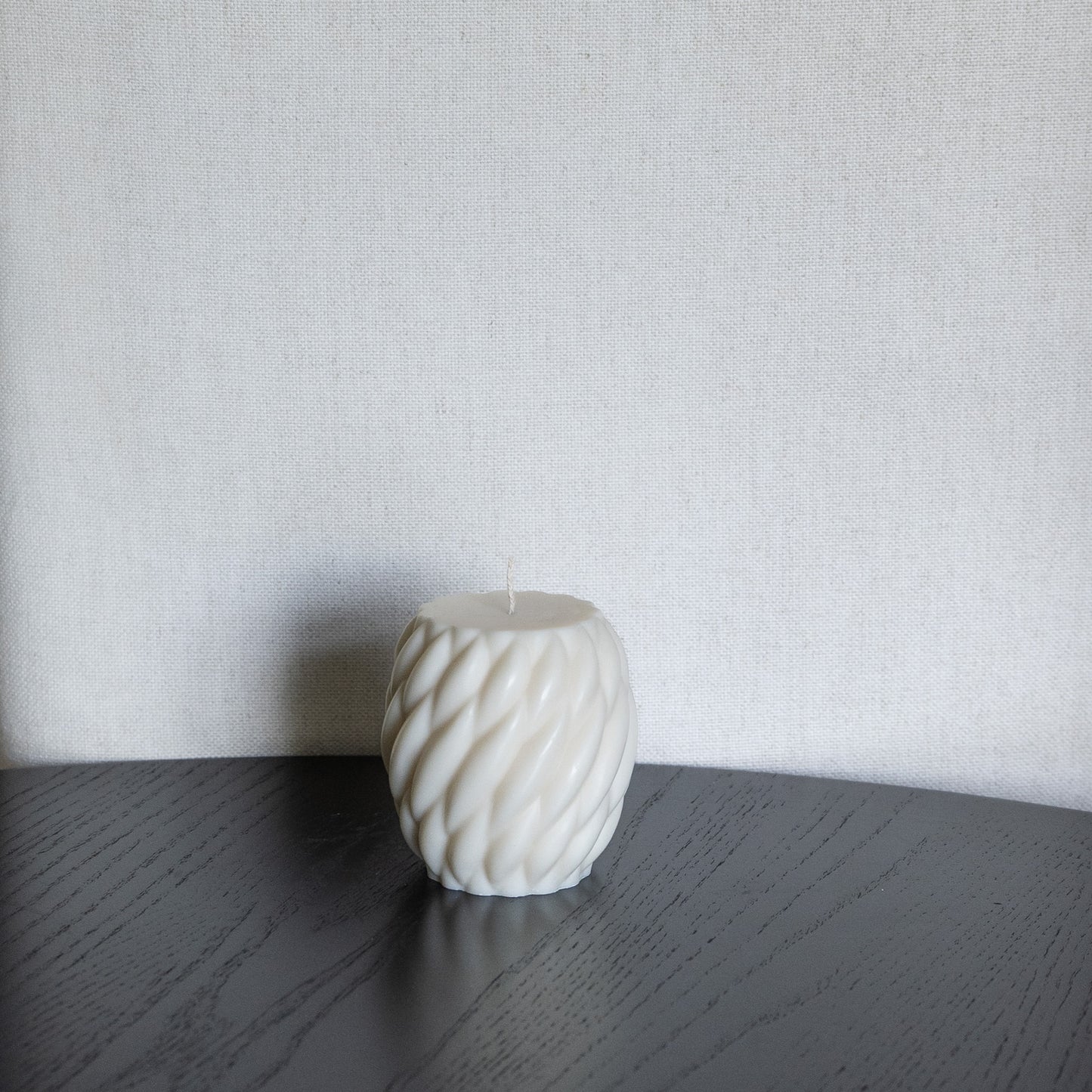 Kerze Knøv in natürlichem Cremeton – skulpturale Designkerzen aus Rapswachs, handgefertigt in Hamburg, 100 % pflanzlich & nachhaltig. Gewebte Struktur, bauchige Form. Dekoriert auf schwarzem Tisch vor hellem Hintergrund.