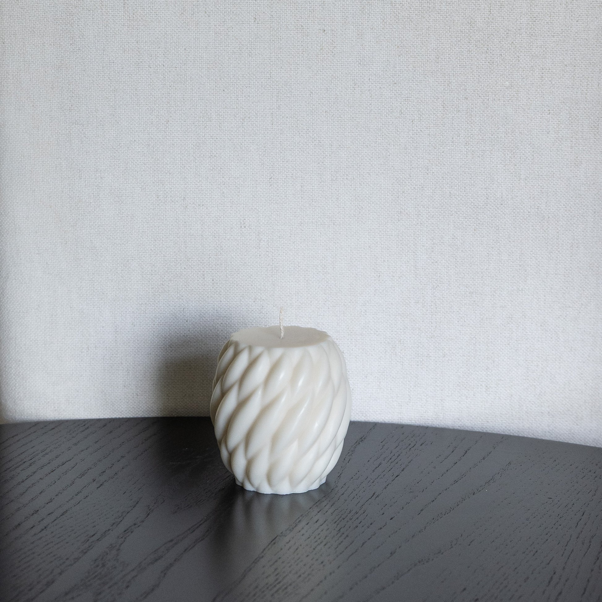 Kerze Knøv in natürlichem Cremeton – skulpturale Designkerzen aus Rapswachs, handgefertigt in Hamburg, 100 % pflanzlich & nachhaltig. Gewebte Struktur, bauchige Form. Dekoriert auf schwarzem Tisch vor hellem Hintergrund.