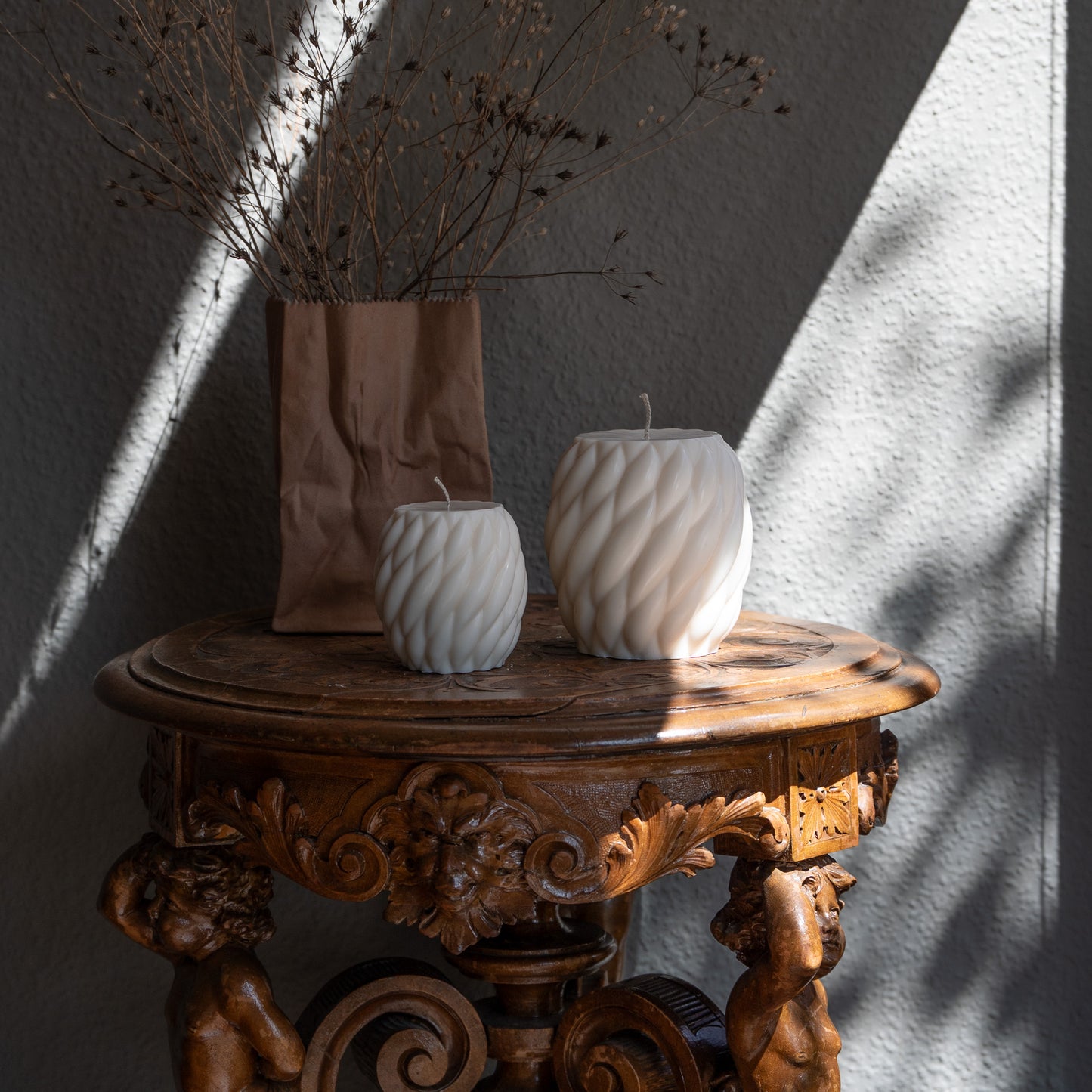 Zweier Kerzen-Set Knøv in natürlichem Cremeton – skulpturale Designkerzen, Rapswachs, handgefertigt in Hamburg, 100 % pflanzlich & nachhaltig. Studio Z. Wellenstruktur, bauchig, gewebt. Dekoriert auf barockem Tisch im Schatten-Lichtspiel der Sonne mit Vase.