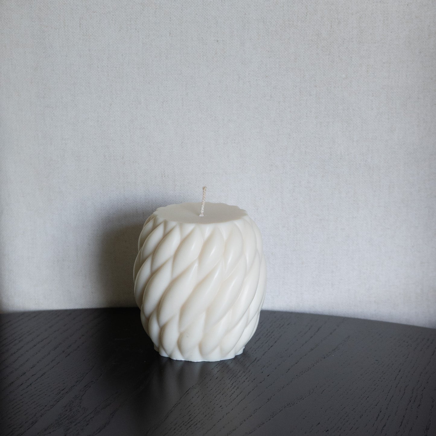 Kerze Knøv in natürlichem Cremeton – skulpturale Designkerzen aus Rapswachs, handgefertigt in Hamburg, 100 % pflanzlich & nachhaltig. Gewebte Struktur, bauchige Form. Dekoriert auf schwarzem Tisch vor hellem Heintergrund.