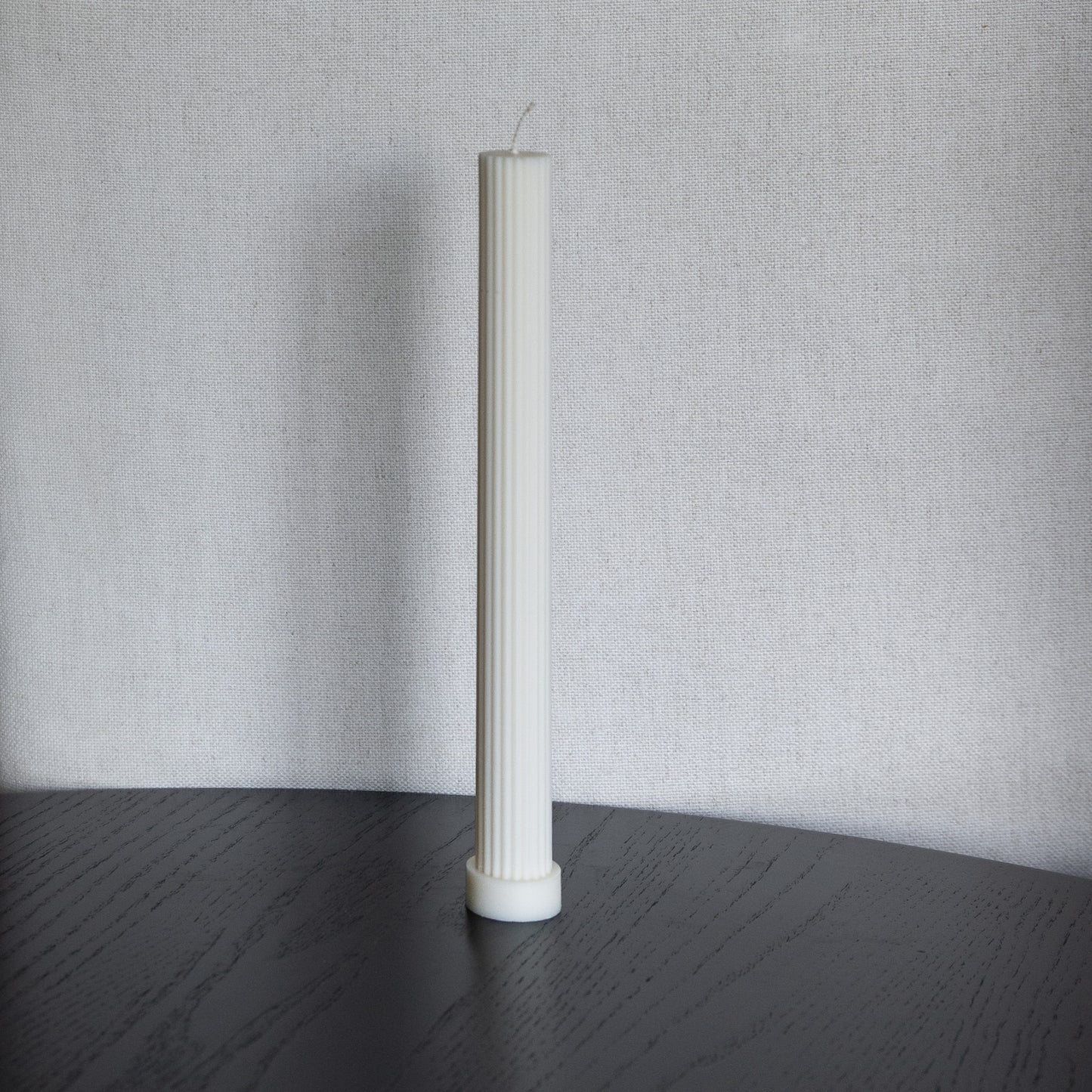 Kerze Lys, geradlininge Stumpenkerze in natürlichem Cremeton – geriffelte längliche Designkerzen, Rapswachs, handgefertigt in Hamburg, 100 % pflanzlich & nachhaltig. Studio Z. Dekoriert auf schwarzem Tisch vor hellem  Hintergrund.