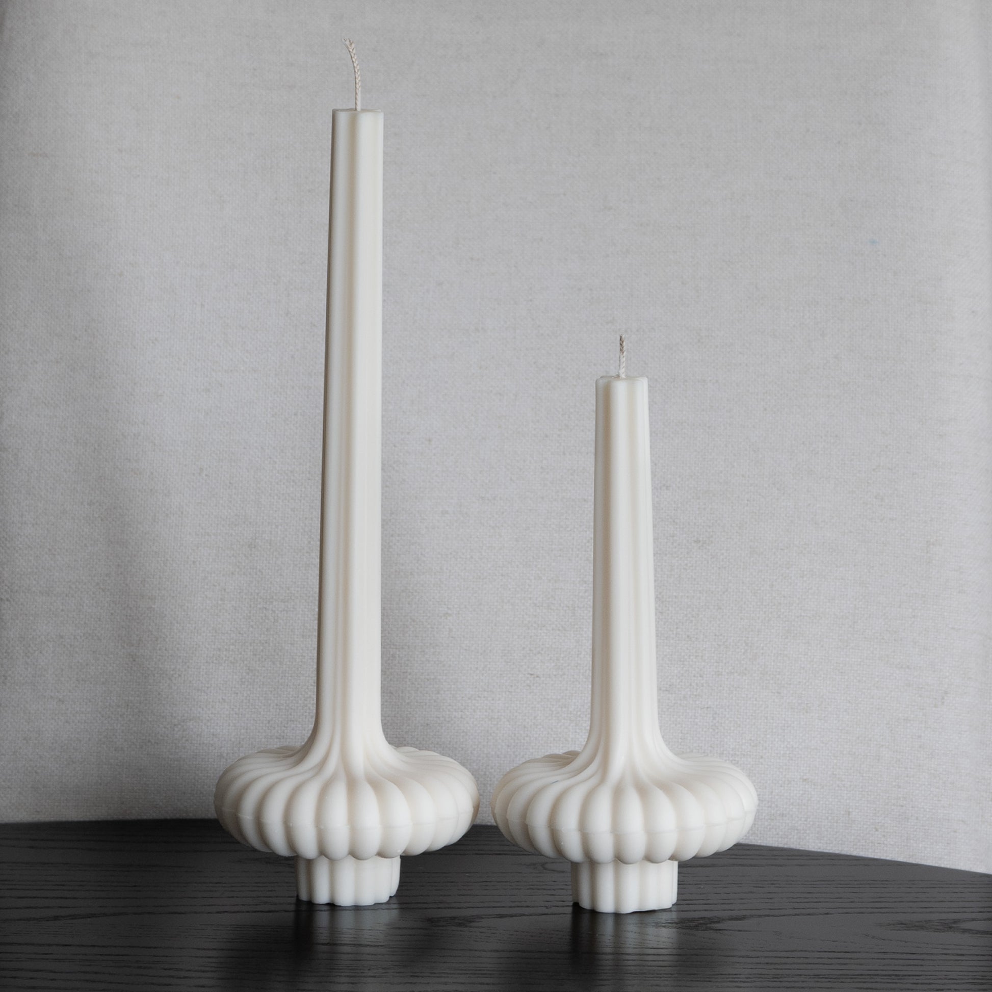 Zweier Set Skæva Kerze in natürlichem Cremeton – skulpturale Designkerzen aus Rapswachs, handgefertigt in Hamburg, 100 % pflanzlich & nachhaltig. Studio Z. Mit plissierter Struktur, markantem Fuß und skulpturaler Form. Dekoriert nebeneinander in zwei Größen auf schwarzem Tisch vor heller Leinenstruktur.