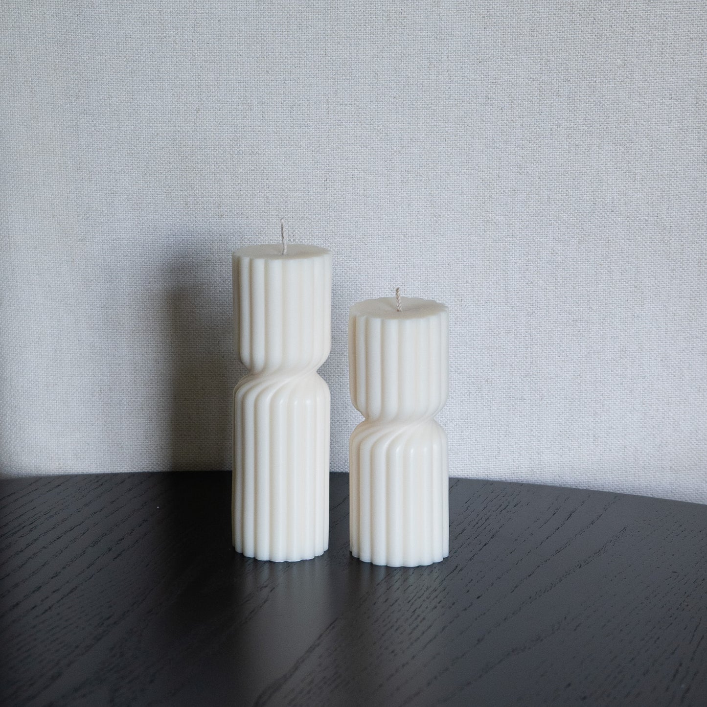 Kerze Strøme gedrehte Stumpenkerze in natürlichem Cremeton – skulpturale längliche Designkerzen, Rapswachs, handgefertigt in Hamburg, 100 % pflanzlich & nachhaltig. Studio Z. Geriffelte Struktur., mittig gedreht Dekoriert auf schwarzem Tisch vor hellem Hintergrund.