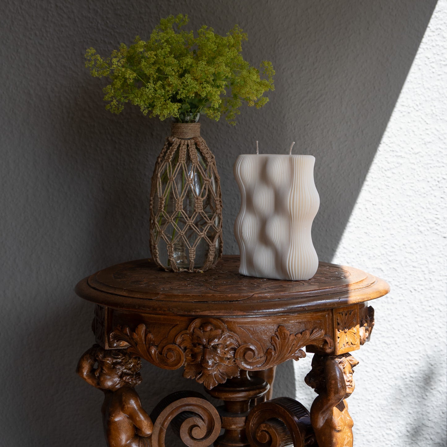 Væg Kerze in natürlichem Cremeton – Designkerzen aus Rapswachs, handgefertigt in Hamburg. 100 % pflanzlich & nachhaltig. Studio Z. Skulpturale Wellenform wie eine horizontale Wachswand. Dekoriert auf barockem Tisch im Schatten-Lichtspiel der Sonne mit Vase und Frauenmantelkraut.