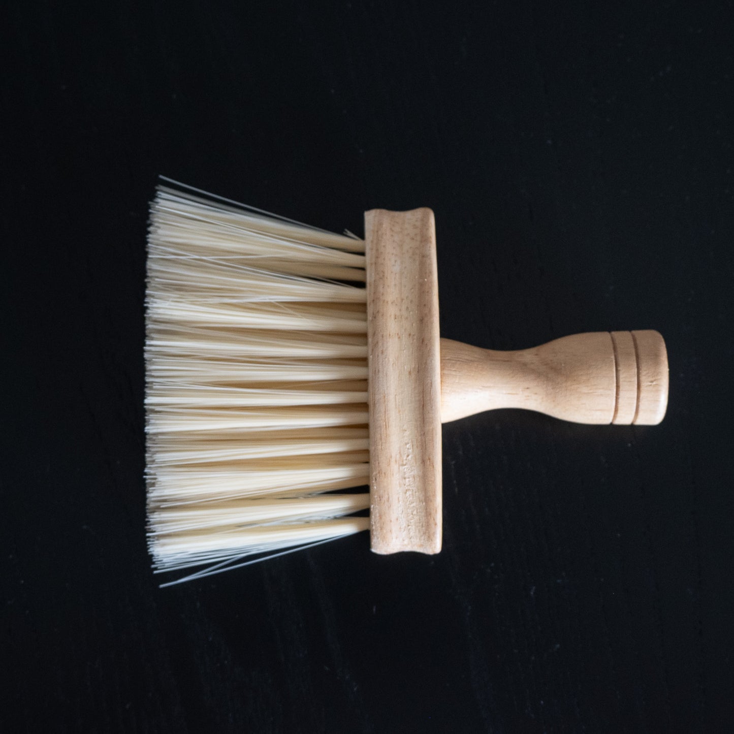 Pflegebürste mit Holzgriff zum Entfernen von Ruß und Staub liegend auf schwarzem Tisch.