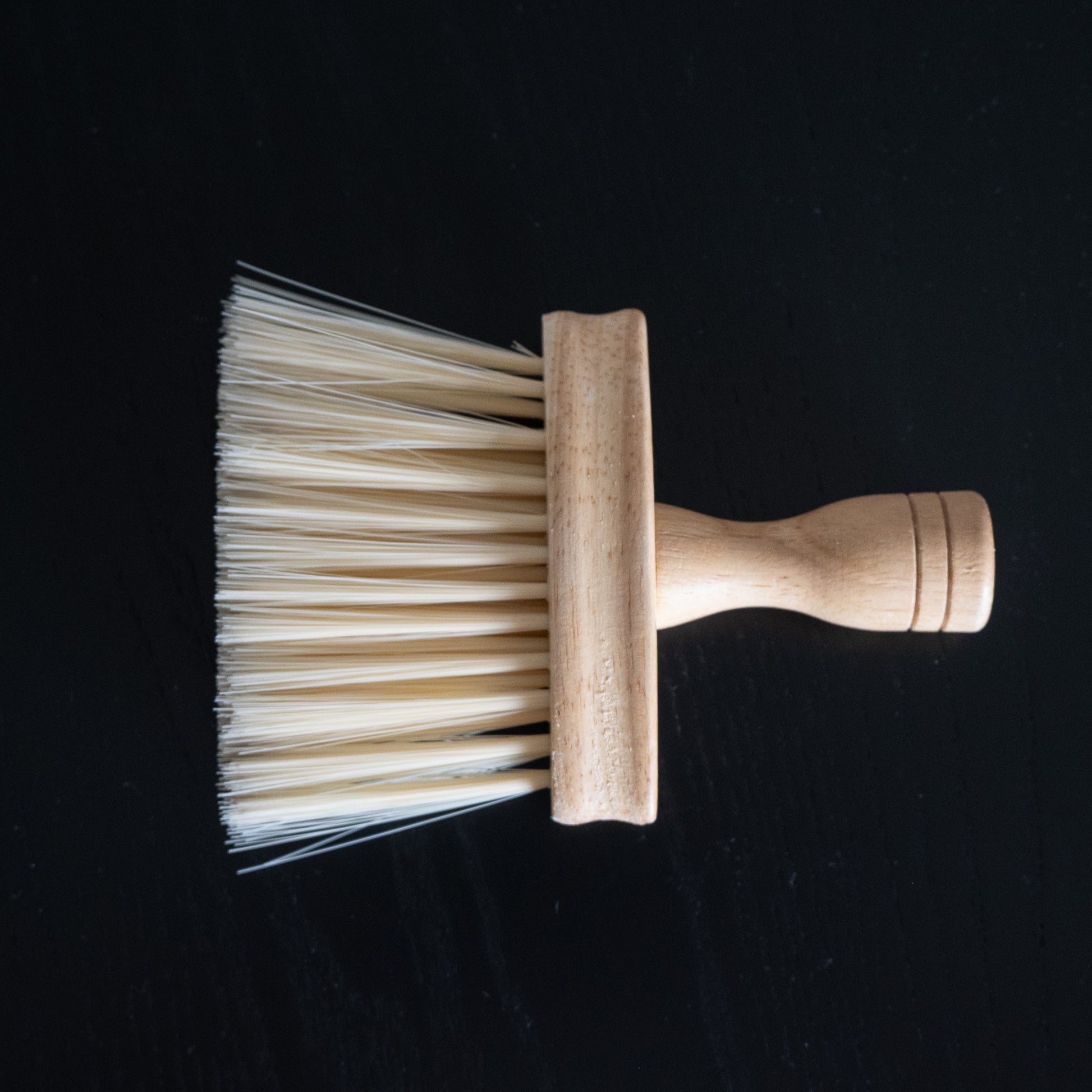 Pflegebürste mit Holzgriff zum Entfernen von Ruß und Staub liegend auf schwarzem Tisch.